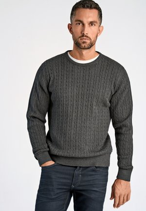 Dark gray cable-knit sweater with a round neck and ribbed cuffs, worn over a white shirt. Notable texture and fitted design.