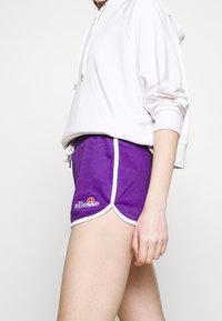 Shorts de sport violets avec un liseré blanc, ornés d'un logo brodé. Associés à un sweat à capuche blanc ample et fabriqués dans un matériau doux.
