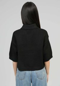 Pull noir à col polo à manches courtes, fabriqué en matériau tricot doux, présentant un ourlet court et des accents côtelés aux poignets et à la taille.