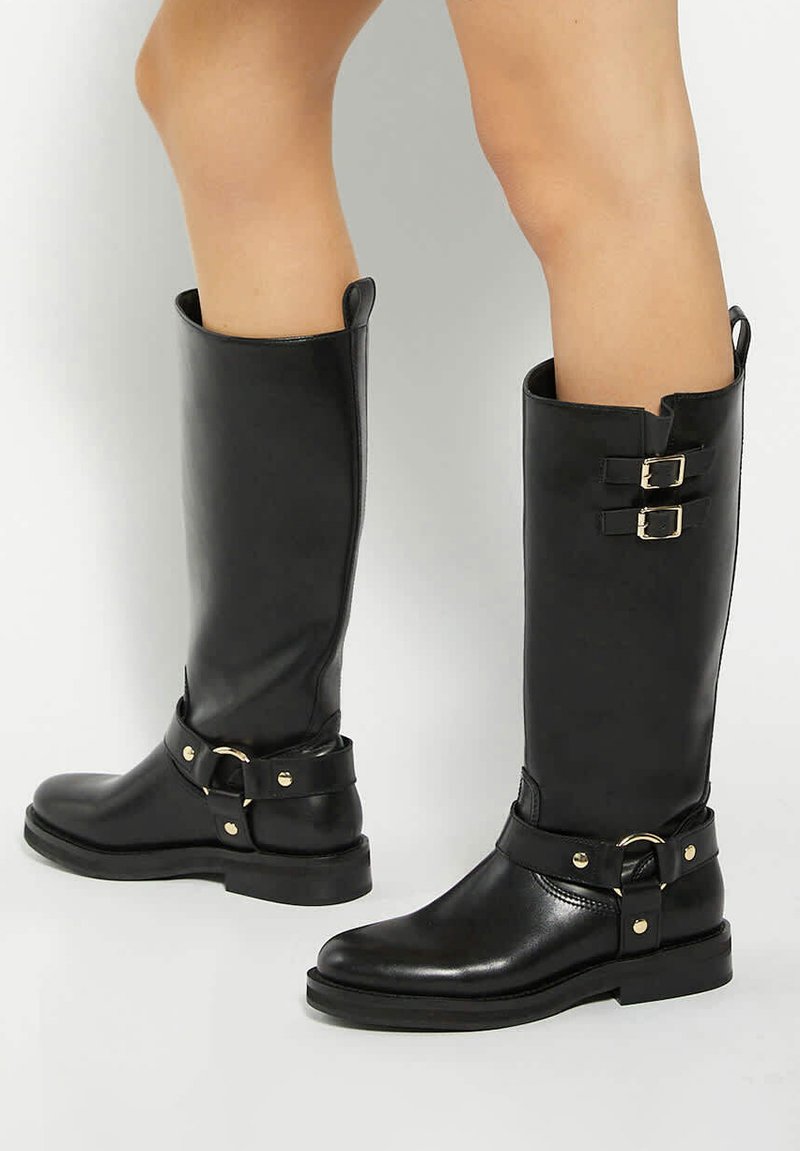 Black mid-calf boots made of smooth leather with a rounded toe, gold hardware accents, dual buckles, and a thick sole with minimal tread.