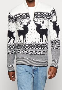 Tröja i vitt och marinblått med zipkrage. Har mönster av renar och snöflingor, strukturerad stickning och ribbade muddar.