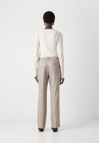 Light long-sleeve top paired with beige plaid trousers featuring a straight cut, side pockets, and a subtle texture. Black footwear completes the look.