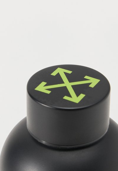 Μαύρο καπάκι μπουκαλιού με τέσσερα πράσινα βέλη που δείχνουν προς τα πάνω, κάτω, αριστερά και δεξιά σε ένα ματ μαύρο δοχείο μπροστά από ένα απλό φόντο.