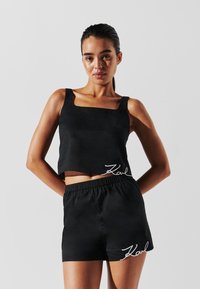 Crni crop top s kvadratnim izrezom i odgovarajuće kratke hlače s elastičnom waistband-om. Ovi artikli imaju bijelu "Karl" izvezeno.