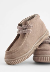 Bottes chelsea en suède marron avec des lacets à double couche et une doublure intérieure texturée, dotées d'une semelle en caoutchouc avec des détails striés.