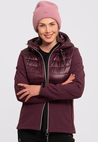 Lilla softshell-jakke med en polstret, skinnende overdel og snoretræk i hætten. Sammen med en lys pink strikket beanie.