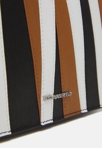 Wielopaskowa torba w kolorach brązowym, czarnym, białym i beżowym, wykonana z materiału przypominającego gumę; posiada tłoczoną fakturę oraz srebrne logo "Karl Lagerfeld".