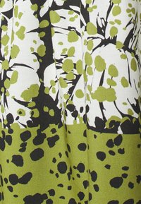 Mönstrad tyg med stora gröna prickar och svarta detaljer på en vit bakgrund, med en texturerad yta och plisserad design.