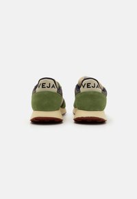 Sko med en grønn semsket hæl, beige overdel og mørkeblå aksenter. "VEJA"-logo på hælen. Designet for komfort med kontrasterende teksturer.