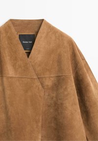 Veste en daim marron clair avec col en V et coutures visibles sur les panneaux des épaules et du devant, avec une étiquette Massimo Dutti.