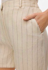 Beige shorts tillverkade av ett texturerat tyg, med vertikala svarta ränder, en framficka och skräddarsydd passform med uppvikta ben.