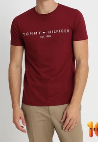 Burgunder kortærmet t-shirt med hvid "TOMMY HILFIGER EST. 1985" tekst. Lavet af blødt stof; tætsiddende design med rund hals.