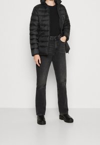 Czarna kurtka puchowa z kapturem, noszona na czarnej koszulce, w połączeniu z ciemnymi dżinsami i czarnymi, masywnymi butami. Gładka tekstura i dopasowany fason.