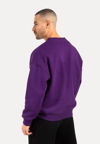 Felpa oversize viola in misto cotone con polsini e orli a coste. Tessuto liscio, design a girocollo e vestibilità comoda.