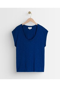 Camiseta de manga corta azul marino con un escote amplio en forma de barco, hecha de una suave y texturizada tela, colgando de una percha de madera sobre un fondo blanco.