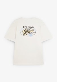 Cremefarvet bomulds t-shirt med løstsiddende pasform, prydet med et grafisk print på bagsiden med teksten "Bare Nyd og Elsk", omkranset af mørkebrun.