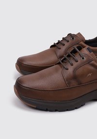Zapatos de cuero marrón con acabado texturizado, puntera redondeada, diseño de cordones y suela de goma con una plantilla intermedia que proporciona soporte.