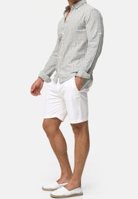 Gestreiftes langärmliges Hemd aus hellgrauem und weißem Stoff, kombiniert mit weißen Shorts. Das Outfit umfasst Slipper mit einer hellbraunen Sohle.