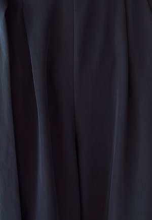 Primo piano di tessuto scuro con pieghe sottili e texture, che mostra materiale drappeggiato in un ambiente neutro.