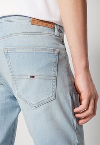 Hellblaue Jeans aus Denim mit einem Lederetikett mit der Aufschrift "JEANS", ausgestattet mit einer Gesäßtasche, die ein kleines Logo in Rot, Weiß und Blau zeigt.