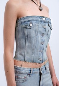 Denimkorsett i ljusblått, med strapless-design, knäppning framtill, bröstfickor och fransad nederkant för en texturerad look.
