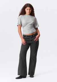 Tricou gri cu mâneci scurte, asortat cu pantaloni evazați negri din denim cu talie înaltă. Textură netedă a țesăturii cu un luciu subtil și o siluetă ajustată.