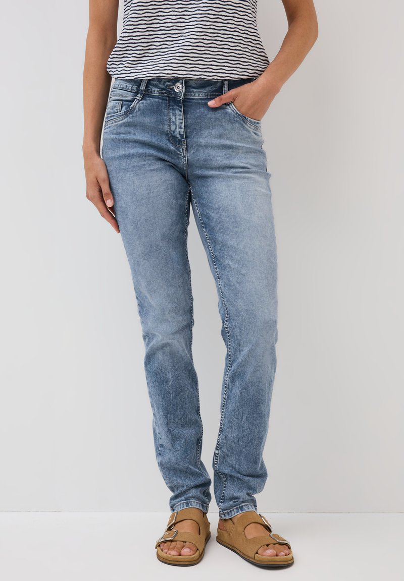 Ljusblå denimjeans med rak passform, fem fickor och en blekt textur, i kombination med bruna sandaler och en randig topp.