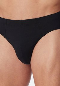 Schwarze Baumwollslip mit niedrigem Bund, elastischem Taillenbund und glatter Textur. Keine sichtbaren Muster oder Hardwaredetails.