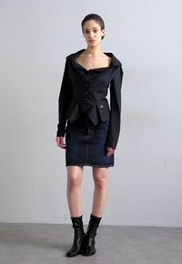 Μαύρο σακάκι peplum με μεγάλο γιακά και κουμπιά μπροστά, σε συνδυασμό με σκούρα τζιν φούστα. Το μοντέλο φορά μαύρες μποτές αστραγάλου. Λείες υφασμάτινες υφές.