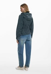 Tumedat denimist jakk, millel on kapuuts, nöörid ja õmmeldud detailid; koos helesiniste laiadest teksadest ja valgetest tossudest.