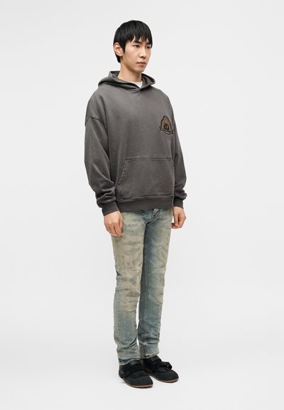 Γκρι φούτερ με κουκούλα και μπροστινή τσέπη με κεντητό σχέδιο, σε συνδυασμό με ανοιχτό μπλε τζιν με φθορές και μαύρα παπούτσια slip-on.