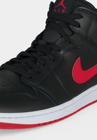 Μαύρο δερμάτινο sneaker high-top με κόκκινο λογότυπο Nike, κόκκινη σόλα, μαύρα κορδόνια και κόκκινο λογότυπο Air Jordan στη γλώσσα.