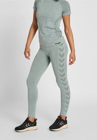 Szary sportowy top z teksturowanymi rękawami oraz dopasowane legginsy z wzorem chevron na boku. Do tego czarne buty sportowe.