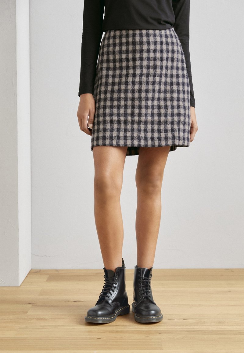 Falda de mezcla de lana a cuadros en azul marino y beige, diseño en A, con un dobladillo que llega a medio muslo, combinada con botas negras de cordones.
