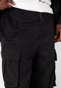 Zwarte cargoshorts van een stof met een gladde textuur, voorzien van zijzakken, een ritszak en een relaxte pasvorm.