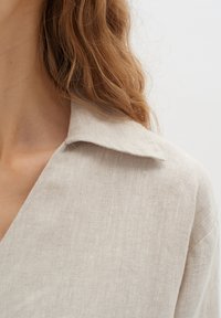Camicia in lino beige chiaro con colletto classico e finitura testurizzata. La fotografia ravvicinata cattura la trama del tessuto e il suo morbido cadere.
