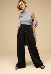Top scurt de culoare gri deschis, pantaloni largi negri cu șnur, croi lejer și sandale; texturi moi și design minimalist.
