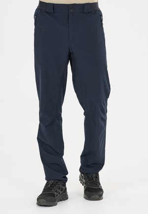 Dunkelblaue Outdoor-Hose mit Reißverschlusstaschen an der Seite, Knopfverschluss und schwarzen Wanderschuhen auf hellem Hintergrund.