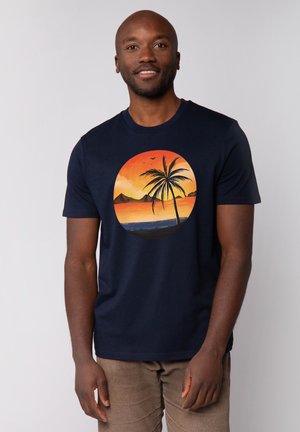 Marineblauw T-shirt met korte mouwen, voorzien van een palmbomenafbeelding binnen een circulair zonsondergangontwerp met oranje, geel en blauwe tinten.