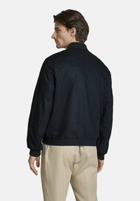 Black bomber jacket with a stand collar, elastic waistband, and long sleeves. Features a smooth, matte texture. Minimalist design.