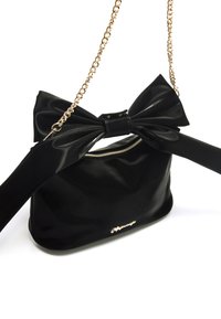 Borsa a tracolla nera lucida con grande fiocco decorativo, catena dorata e chiusura con zip. Presenta una texture liscia e un dettaglio del logo sulla parte anteriore.