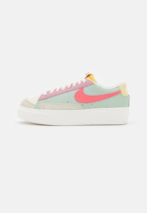 Low-profile sneaker with pastel green body, pink accents, red Nike swoosh, white laces, beige toe cap, and thick white sole.