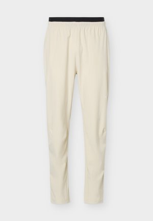 Béžové kalhoty slim fit s černým elastickým pasem, vyrobené z lehké, hladké látky, vhodné pro běžné i sportovní nošení.