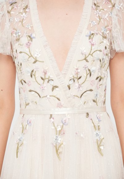 Šaty s kvetinovou výšivkou z ľahkého béžového tylu, s hlbokým výstrihom do V, priehľadnými volánovými rukávmi a saténovým pásom s dekoratívnymi vzormi.