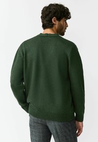 Donkergroene gebreide trui met een ronde hals, geribbelde manchetten en zoom. Gestructureerde afwerking, losse pasvorm en een naaddetail aan de achterkant.