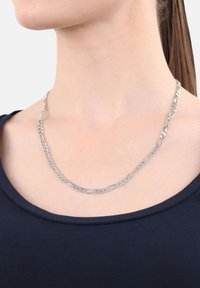 Collar de cadena de plata con eslabones ovalados alargados y eslabones de curb, llevado en el cuello de una mujer, combinado con una blusa de color azul marino.