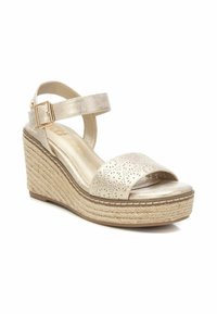 Sandalo wedge con tomaia in oro metallico, punta aperta, cinturino alla caviglia e base in juta intrecciata. Il cinturino presenta dettagli floreali per perforazione.