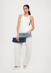White tank top, light blue and white high-waisted jeans, navy clutch with textured detail, and white pointed-toe shoes.