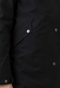Zwarte outerwear met een gladde textuur, voorzien van zilveren knopen en een ontwerp met opgevouwen zakflappen. De stiksels zijn minimaal en elegant.