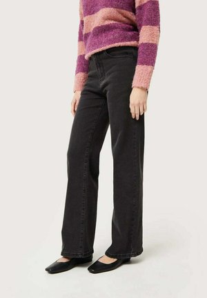 Jeans de tiro alto negros con diseño de pierna recta, que cuentan con bolsillos frontales y detalles de costura, combinados con un suéter a rayas de color rosa y púrpura.